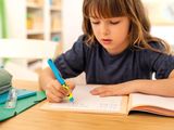 a young girl sitting at a table writing in a book