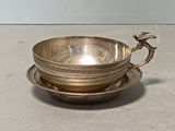 un bol et une soucoupe en métal argenté posés sur une soucoupe, sur une table