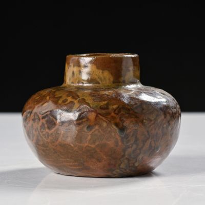 un vase marron posé sur une table sur fond noir