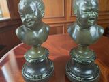 two bronze busts of children on pedestals on a table