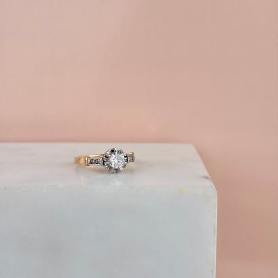 a gold engagement ring with two diamonds on top of a white marble block
