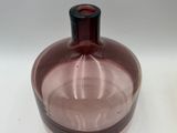 purple glass bottle with a black top sitting on a white surface