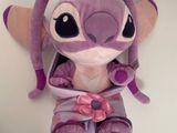peluche violette assise sur une surface blanche, avec un nœud rose