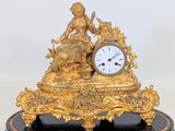 a gold clock sitting on a black base with a woman on it