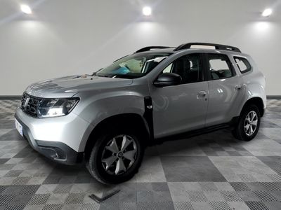 La Dacia argentée est garée dans une grande pièce au sol carrelé en damier.