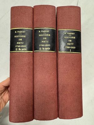 Une main tient trois livres rouges à la couverture noire