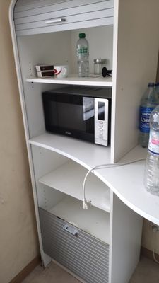 a microwave on a shelf with a bottle of water on top of it