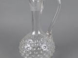 a clear glass vase with a handle on a gray surface