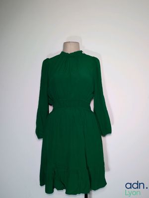 La robe verte est posée sur un support de mannequin devant un mur blanc.