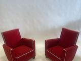 pair of red leather lounge chairs with white piping on the arms