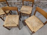 four wooden chairs with wicker seats sit in front of a brick wall