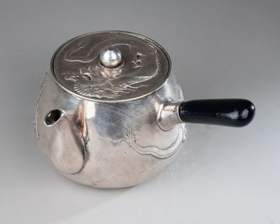 a silver tea pot with a black handle on a white table