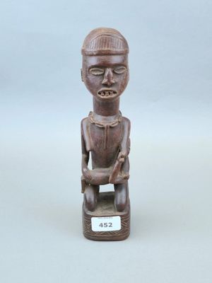 statue en bois représentant un homme assis sur un tabouret, tenant une étiquette à la main
