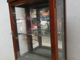 une vitrine en bois avec des étagères en verre, placée dans un coin