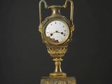 une horloge dorée posée sur un support, elle-même posé sur une table blanche