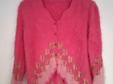 Le pull est rose et orné de broderies dorées.