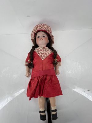 une poupée vêtue d'une robe rouge et d'un chapeau, posée sur un socle
