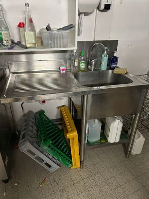 a sink in the corner of a kitchen with a lot of cleaning supplies