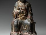 une vieille statue représentant un homme assis sur un tabouret