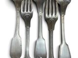 six cuillères en argent et une fourchette posées sur un plateau blanc