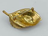 an image of a gold leaf brooch on a white surface
