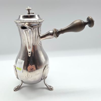 une cafetière ancienne en argent, dotée d'une poignée en bois, posée sur un support blanc