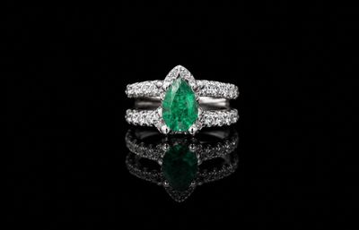 un gros plan d'une bague sertie d'une émeraude verte et de diamants, posée sur une surface noire
