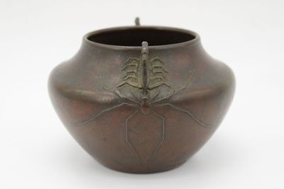 un vase marron orné d'une araignée, posé sur un fond blanc