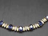 a gold necklace with blue and white beads on a black surface