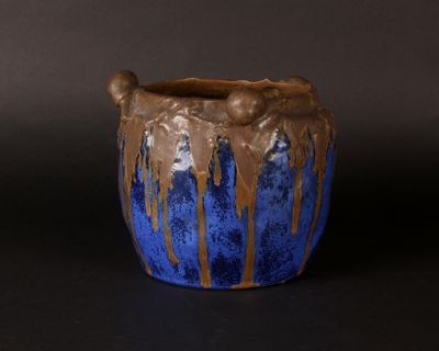 a blue and brown vase with a brown handle on a black surface