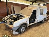une camionnette blanche dont le capot est cassé, garée dans une grange