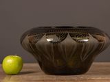 an apple sitting next to a black vase on a wooden table