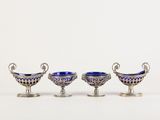 trois plats en verre argenté et bleu posés sur des socles, disposés sur une surface blanche