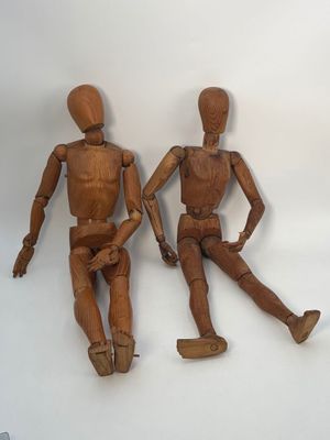 deux mannequins en bois assis l'un à côté de l'autre sur une surface blanche