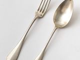 two silver spoons and a fork on a white surface