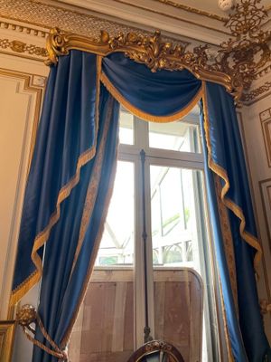 a blue curtain with gold trim and a mirror in a room