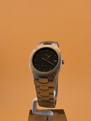 une montre noire et dorée posée sur un socle, sur fond jaune