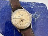 une vieille montre avec un bracelet en cuir marron posée sur une plaque de marbre bleu