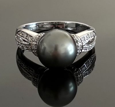 a black pearl and diamond ring on a black surface