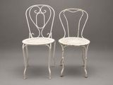 pair of white iron garden chairs on grey background