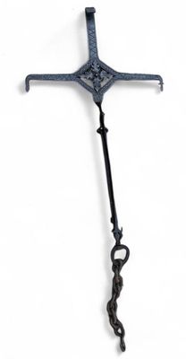 an old iron cross hanging from a chain on a white wall
