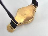 a gold watch on a black cord on a white surface