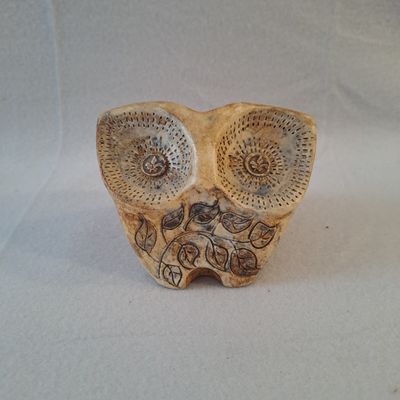 une petite figurine de chouette posée sur une surface blanche