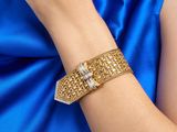 La femme porte une robe bleue et un bracelet doré.