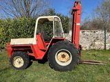 a red tractor parked in the grass near a stone wall