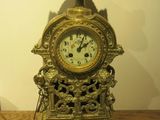 a gold clock sitting on a wooden table with a vase on top