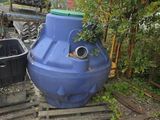 un grand réservoir d'eau bleu posé à côté d'une poubelle noire