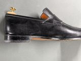 black leather loafer shoes with gold buckles on a gray surface