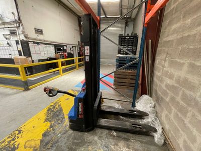 Le chariot élévateur est garé dans l'entrepôt, avec des cartons posés au sol.