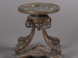 une table ancienne en bronze avec un plateau en verre, sur fond gris